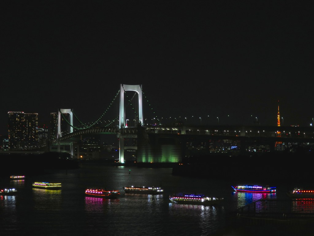 View of the Rainbow Bridge from Odaiba with many lit up pleasure boats